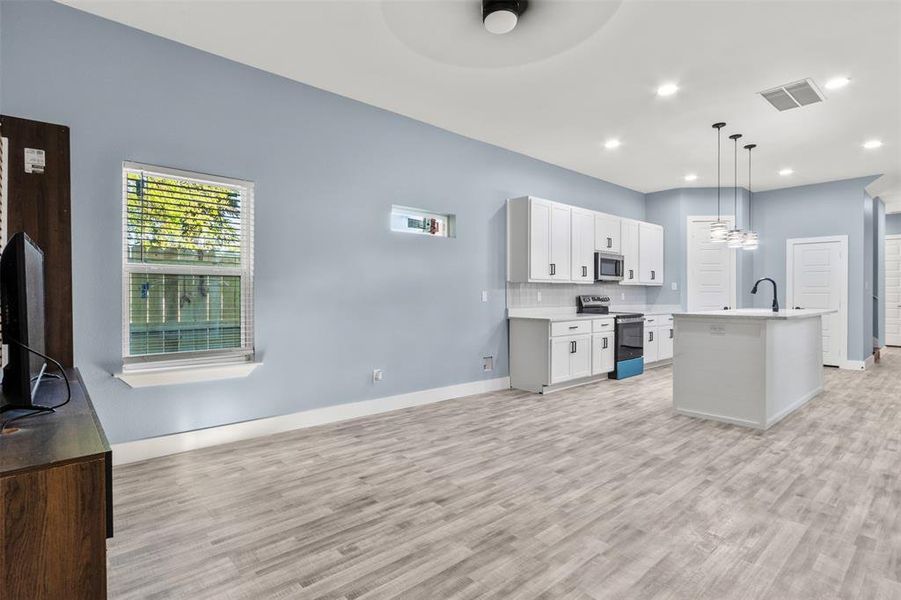 Kitchen featuring white cabinets, a kitchen island with sink, light wood-type flooring, decorative light fixtures, and stainless steel appliances