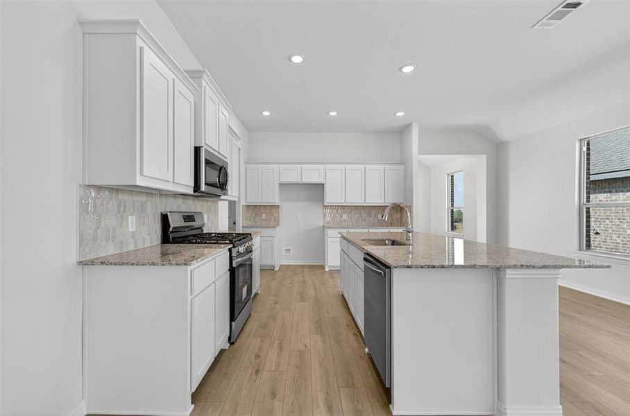 Kitchen featuring appliances with stainless steel finishes, white cabinetry, light stone counters, tasteful backsplash, and a kitchen island with sink