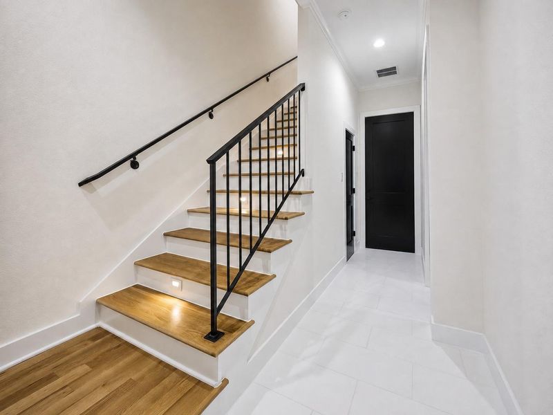 The interior staircase makes a stylish first impression with warm wood treads, crisp white risers, and sleek black iron railings. Integrated step lighting adds both function and atmosphere, while recessed lighting brightens the adjoining hallway. Black interior doors create dramatic contrast against the soft neutral walls, reinforcing the home’s sophisticated contemporary design. The interior staircase makes a stylish first impression with warm wood treads, crisp white risers, and sleek black iron railings. Integrated step lighting adds both function and atmosphere, while recessed lighting brightens the adjoining hallway. Black interior doors create dramatic contrast against the soft neutral walls, reinforcing the home’s sophisticated contemporary design.