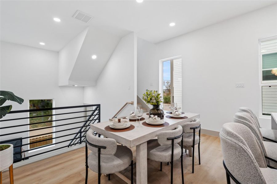 Overlooking the dramatic two-story living room, this open dining area features modern railing details, recessed lighting, and wide-plank SPC flooring—blending form and function in an architecturally distinct layout.