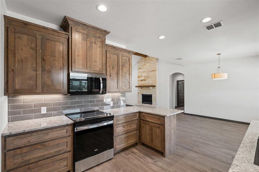 Kitchen with stainless steel appliances, a peninsula, arched walkways, light wood finished floors, and tasteful backsplash