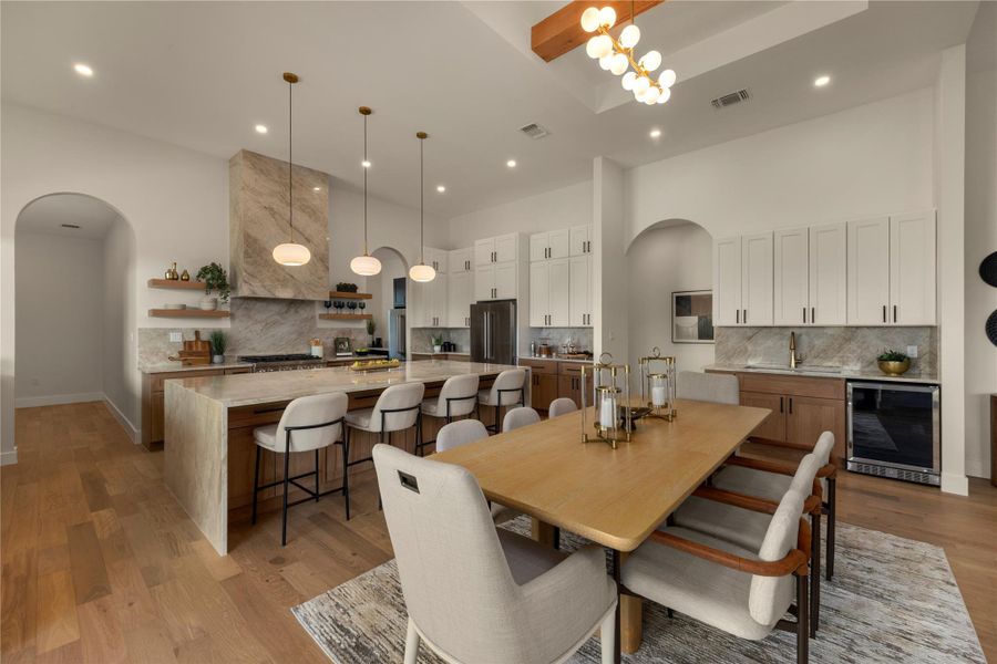 Dining room with arched walkways, beverage cooler, light wood-style floors, a chandelier, and a high ceiling