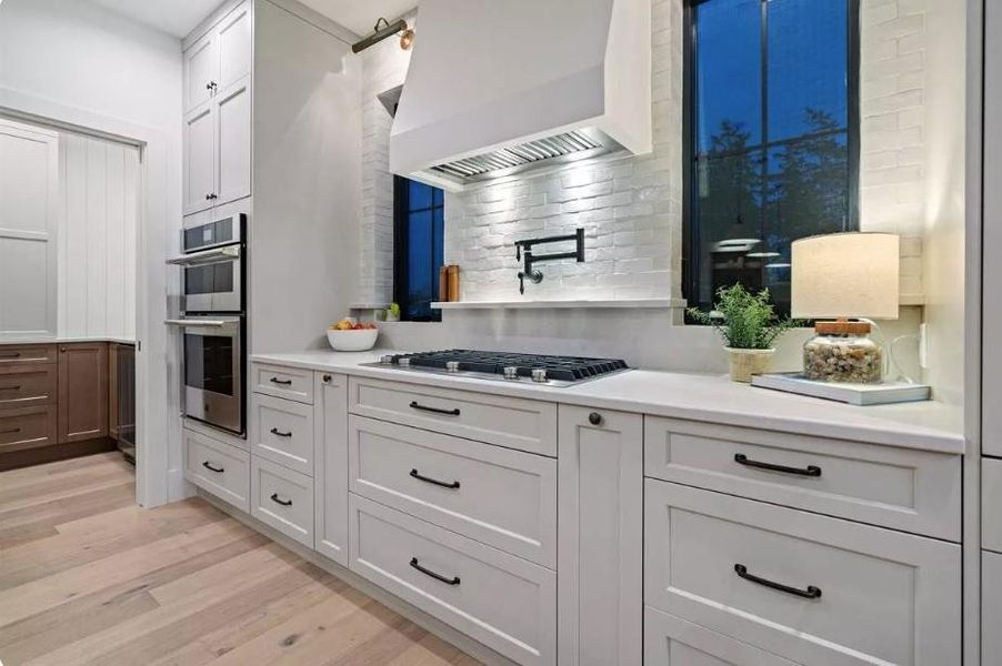 Kitchen stainless steel appliances, Shaker White cabinetry, custom Ventahood, Windows to allow for Natural light and White painted Brick Backsplash