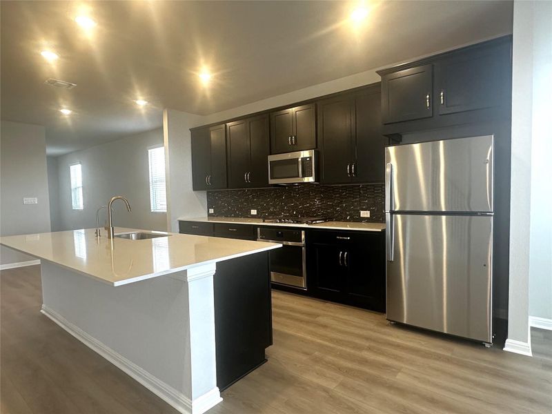 Kitchen featuring stainless steel appliances, center island, elegant backsplash, and brass colored fixtures Kitchen featuring stainless steel appliances, center island, elegant backsplash, and brass colored fixtures