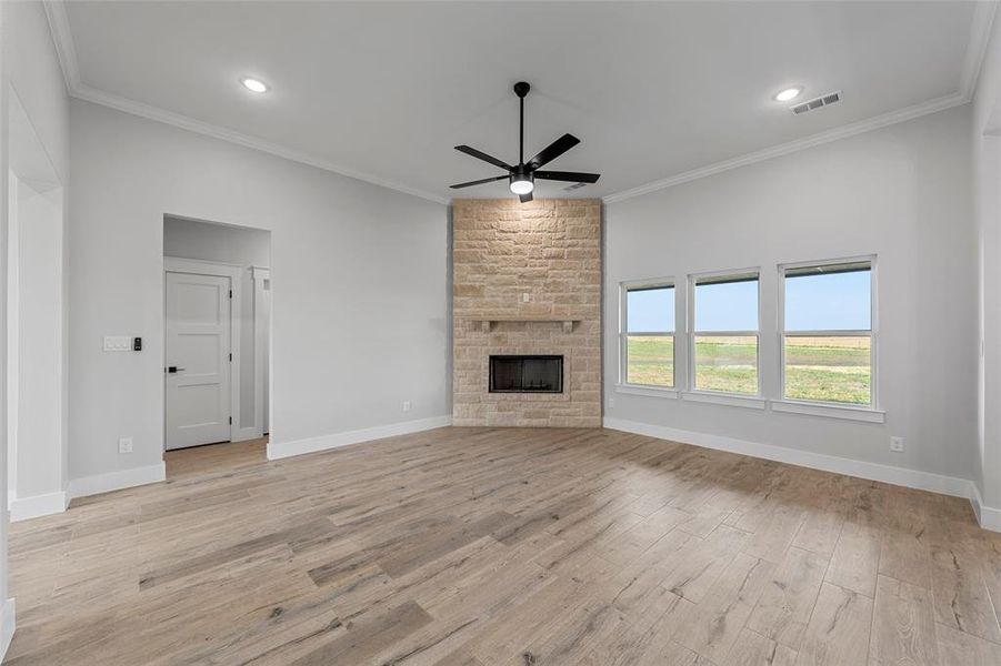 Unfurnished living room with a stone fireplace, crown molding, light wood-type flooring, and ceiling fan