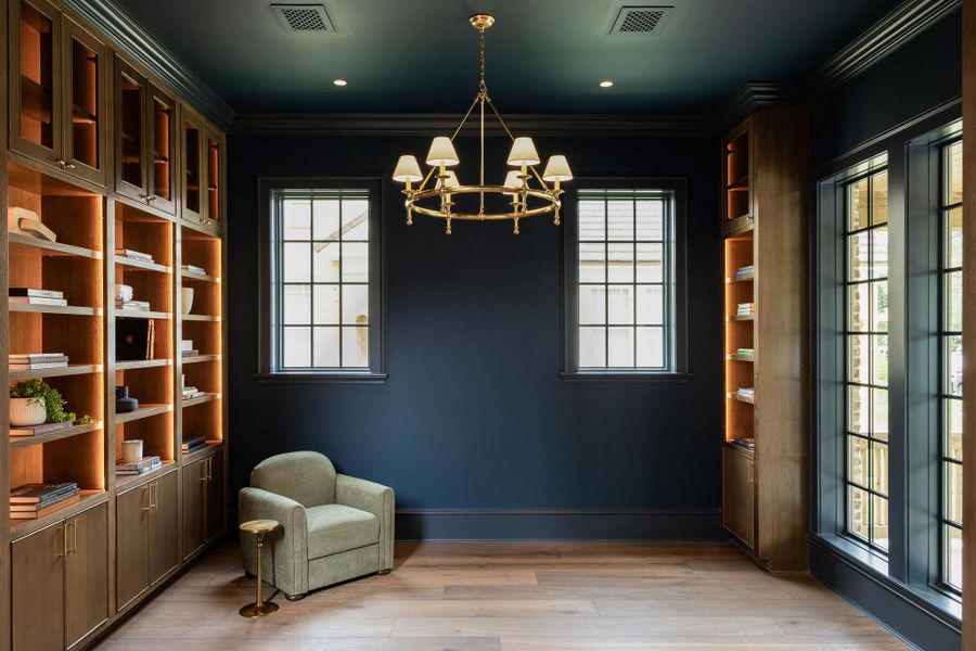 Dramatic library with deep navy walls and ceiling, floor-to-ceiling custom wood built-ins with interior accent lighting on both sides, brass chandelier, recessed downlights, gridded Pella windows with black interior frames, and wide-plank hardwood floors. French doors with black-framed gridded glass open to an adjacent space. Dramatic library with deep navy walls and ceiling, floor-to-ceiling custom wood built-ins with interior accent lighting on both sides, brass chandelier, recessed downlights, gridded Pella windows with black interior frames, and wide-plank hardwood floors. French doors with black-framed gridded glass open to an adjacent space.