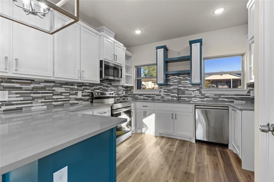 Kitchen with open shelves, stainless steel appliances, white cabinets, light wood-style floors, and tasteful backsplash