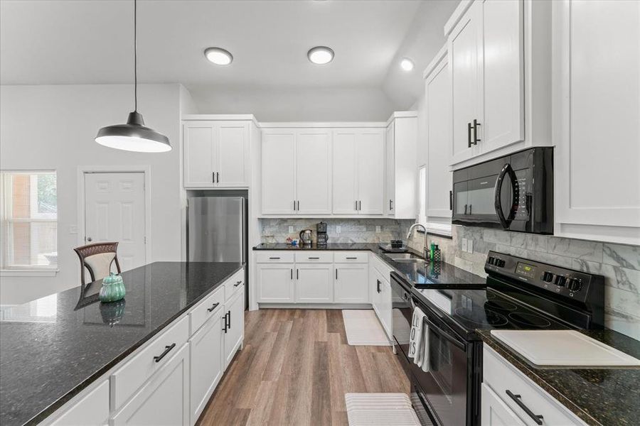 Kitchen featuring black appliances, dark stone countertops, white cabinetry, and decorative light fixtures
