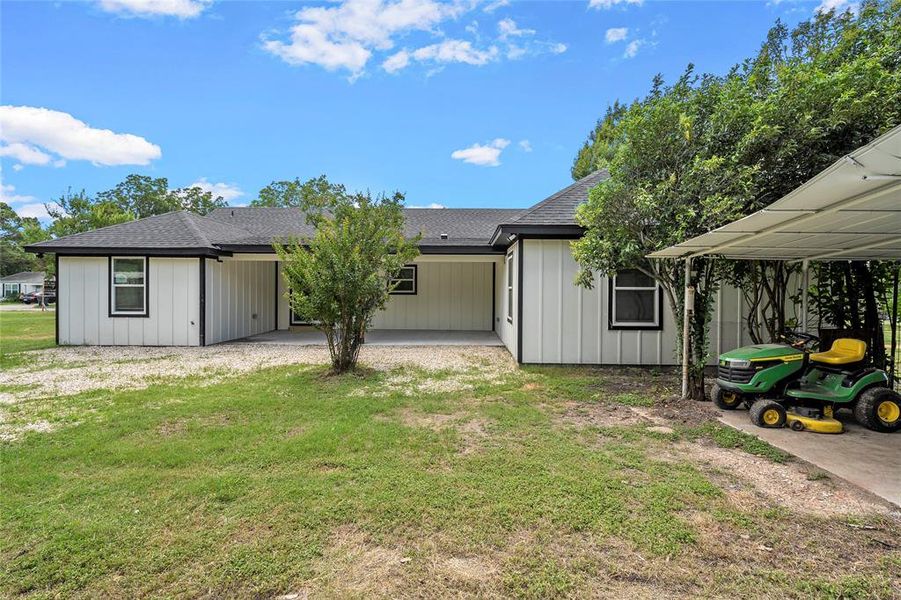 Rear exterior featuring white board and batten siding with black trim, a covered patio, and a covered carport structure Rear exterior featuring white board and batten siding with black trim, a covered patio, and a covered carport structure