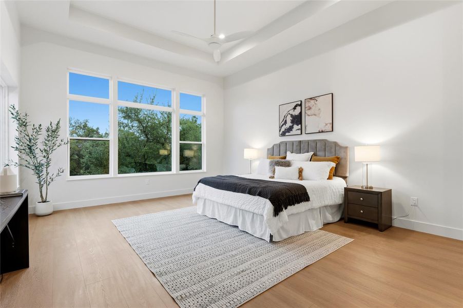 Bedroom with light wood-style flooring, a tray ceiling, and ceiling fan