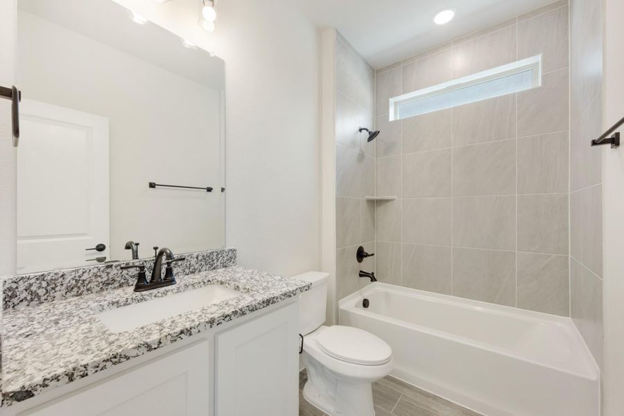 Bathroom with granite countertop vanity, white tub, and tiled shower surround with small window