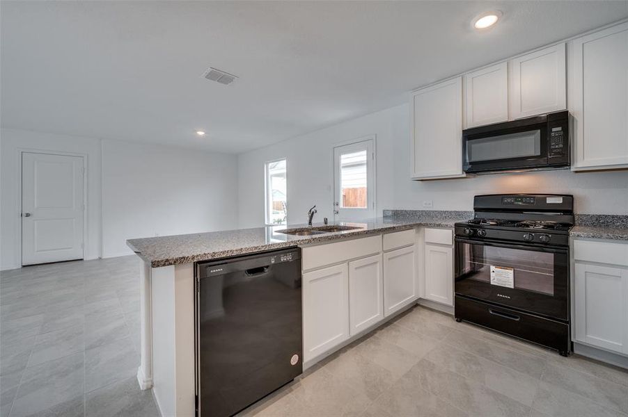 Kitchen with white cabinetry, black appliances, light tile floors, and kitchen peninsula Kitchen with white cabinetry, black appliances, light tile floors, and kitchen peninsula