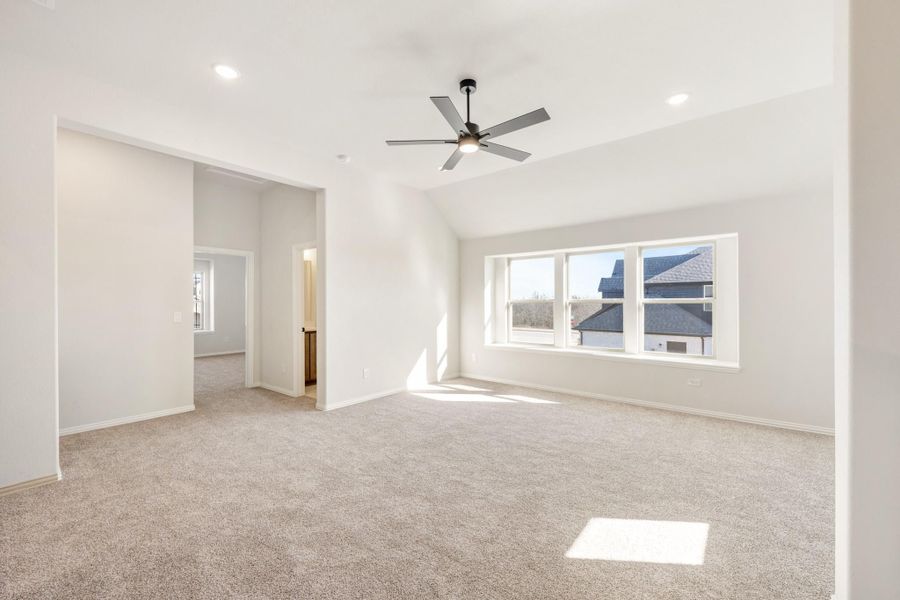Empty bedroom with vaulted ceiling, ceiling fan, carpet flooring, and large windows