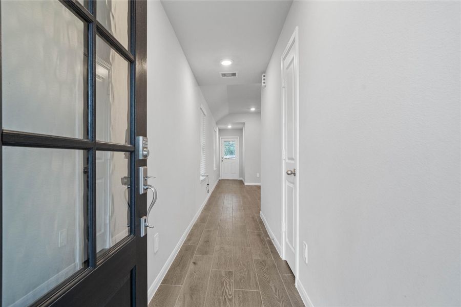This entryway features a modern, open-concept design. The long, bright corridor utilizes a neutral color palette, recessed lighting, and floor tiles to lead the eye toward the home's main living area.
