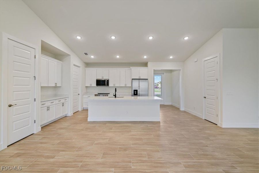 Kitchen featuring lofted ceiling, white cabinetry, stainless steel appliances, an island with sink, and recessed lighting