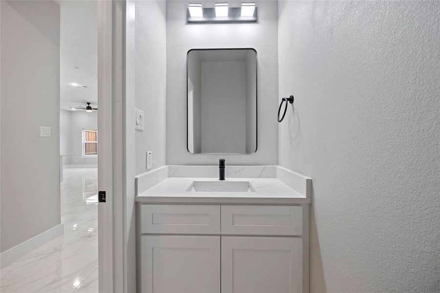 Bathroom with baseboards, a textured wall, marble finish floor, vanity, and a ceiling fan