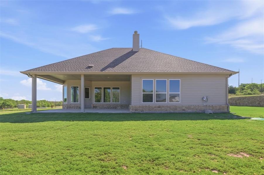 Rear view of property with a lawn, a patio area, roof with shingles, a chimney, and brick siding