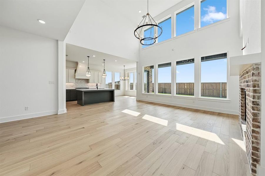 Unfurnished living room with a chandelier, light wood-type flooring, recessed lighting, a fireplace, and a towering ceiling
