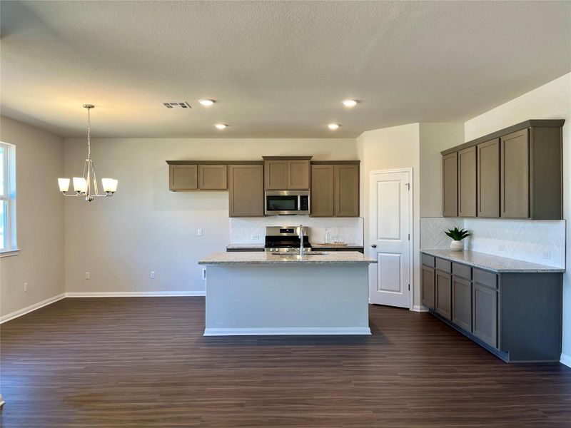 Kitchen featuring light stone countertops, hanging lights, stainless steel appliances, and dark wood-type flooring