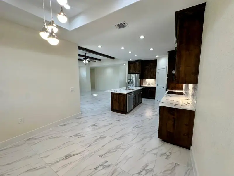 Kitchen with a center island with sink, decorative backsplash, open floor plan, light stone countertops, and recessed lighting