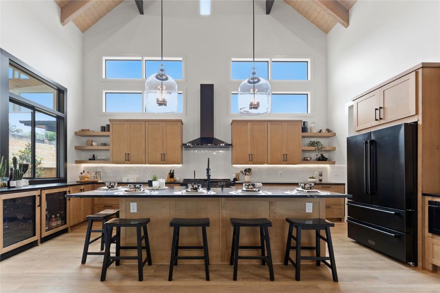 Vaulted ceiling kitchen featuring exposed wood beams, light wood-finish cabinetry, a large kitchen island with counter seating, a black appliance suite, and a beverage cooler Vaulted ceiling kitchen featuring exposed wood beams, light wood-finish cabinetry, a large kitchen island with counter seating, a black appliance suite, and a beverage cooler