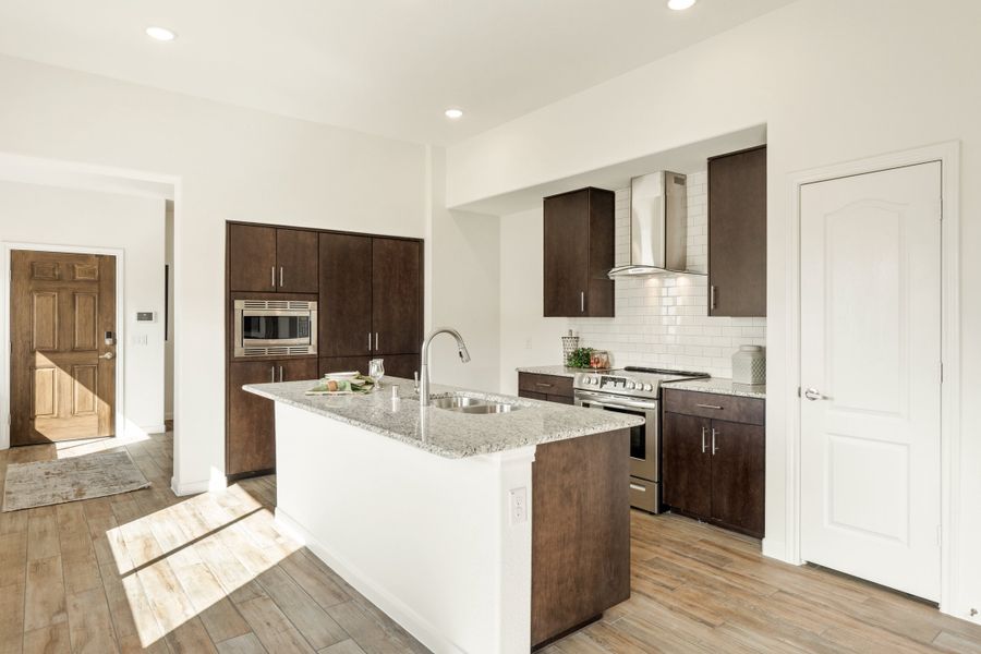 Kitchen with dark wood cabinets, granite island with sink, stainless steel appliances, and white subway tile backsplash on wood-look floors