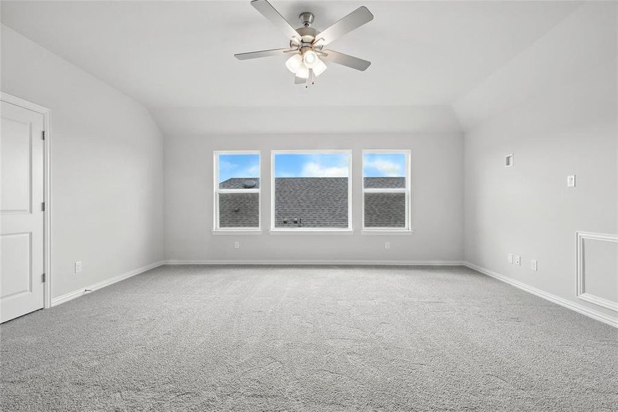 Carpeted empty room featuring vaulted ceiling and a ceiling fan Carpeted empty room featuring vaulted ceiling and a ceiling fan