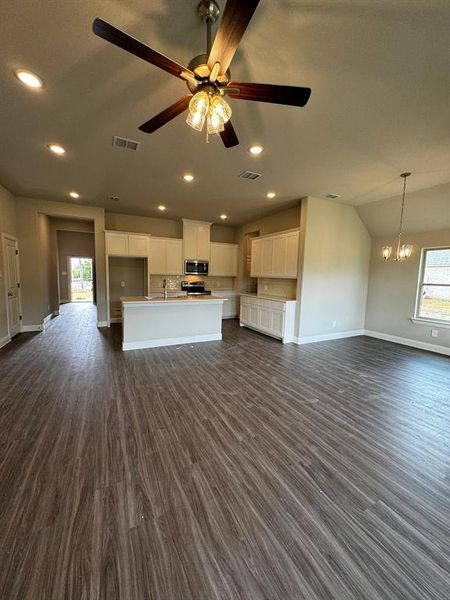 Unfurnished living room featuring dark hardwood / wood-style flooring, ceiling fan with notable chandelier, vaulted ceiling, and sink