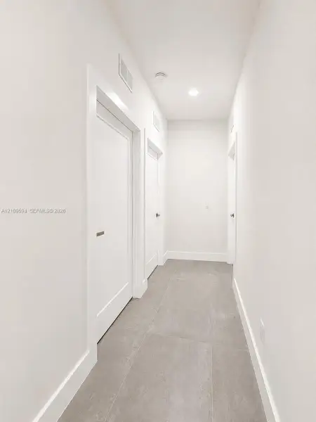 Hallway featuring large-format ceramic tile flooring, neutral wall finishes, recessed ceiling lighting, and multiple interior doors with modern hardware