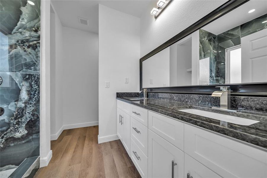 Bathroom with a marble finish shower, double vanity, and light wood-style flooring