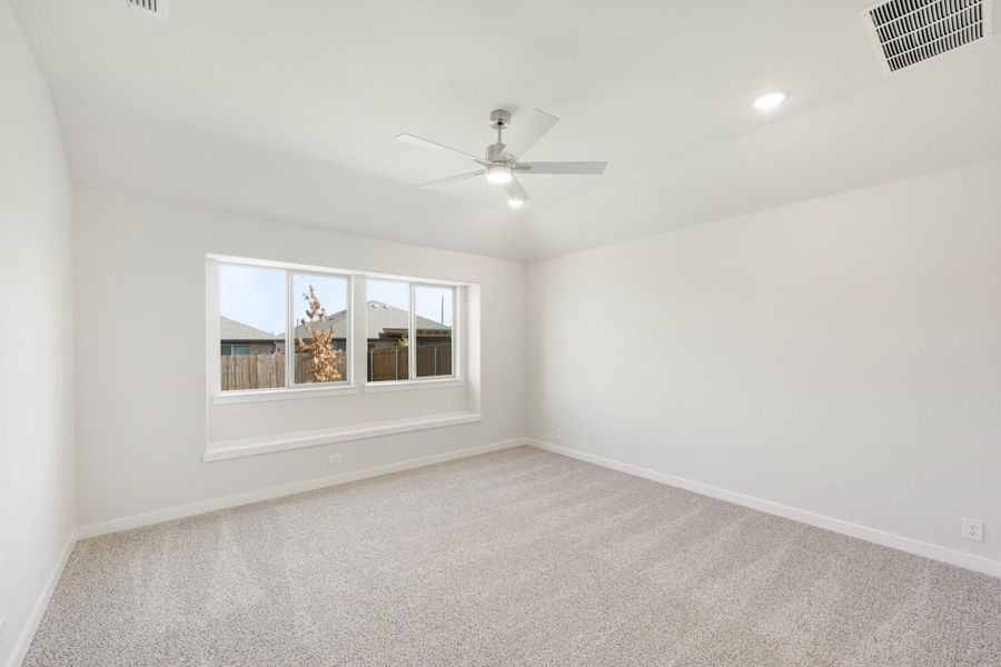 Empty bedroom with white walls, ceiling fan, carpet flooring, and a large window with backyard view