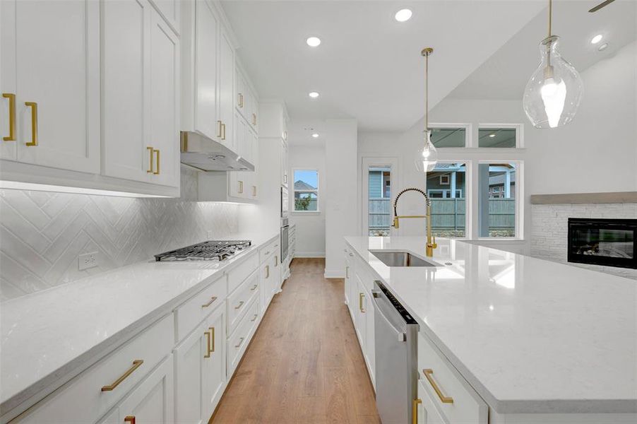 The contemporary kitchen features white cabinetry with gold-toned hardware, white countertops, a gas cooktop, and a double basin sink with a gold-toned faucet