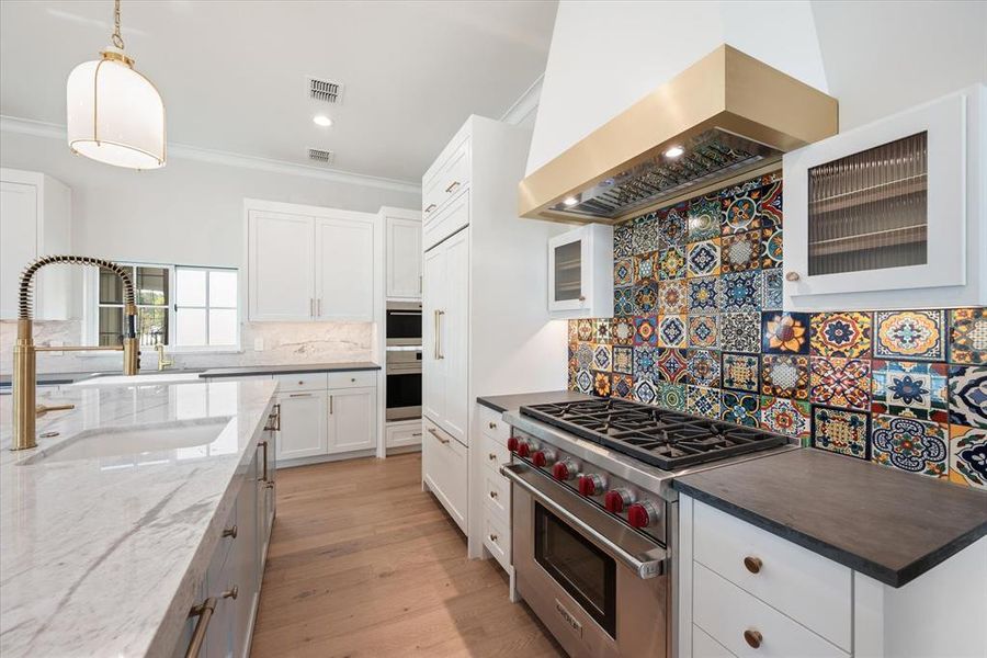 Kitchen with decorative tile backsplash, Kohler sink, custom exhaust hood, Sub Zero stove, white countertops, and white cabinets