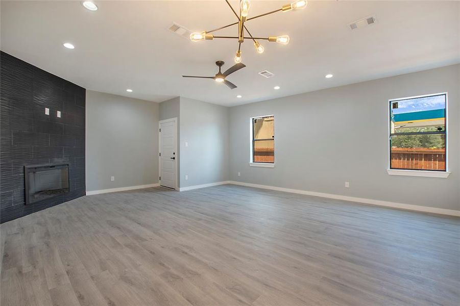 Unfurnished living room with hardwood / wood-style floors, a tiled fireplace, and ceiling fan with notable chandelier