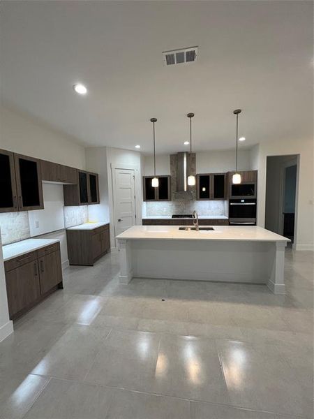 Kitchen featuring backsplash, dark brown cabinets, sink, exhaust hood, and a center island with sink