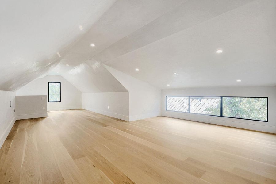 A spacious attic retreat features warm hardwood flooring, recessed lighting, and ample natural light from its unique window configurations.