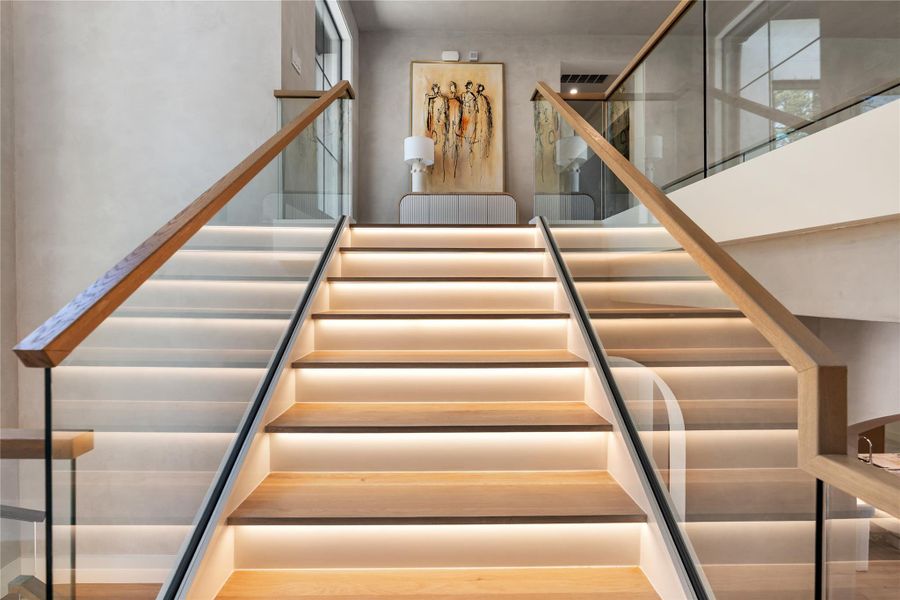A striking staircase featuring glass and illuminated treads, complemented by white oak threads and matching handrails. A striking staircase featuring glass and illuminated treads, complemented by white oak threads and matching handrails.