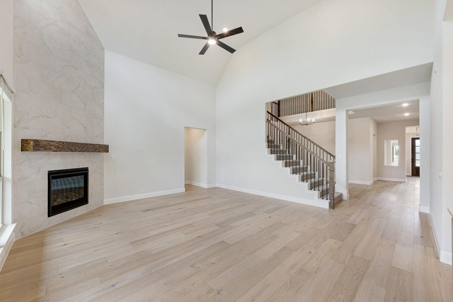 Open living room with vaulted ceiling, stone fireplace, hardwood floors, and staircase with iron balusters Open living room with vaulted ceiling, stone fireplace, hardwood floors, and staircase with iron balusters