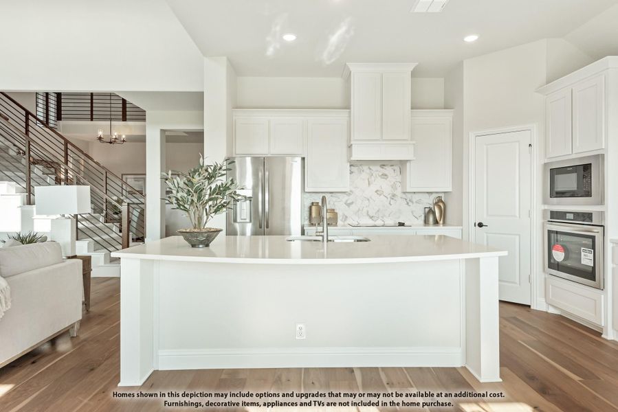 White kitchen with large curved island, stainless steel appliances, marble backsplash, and hardwood floors open to living area White kitchen with large curved island, stainless steel appliances, marble backsplash, and hardwood floors open to living area