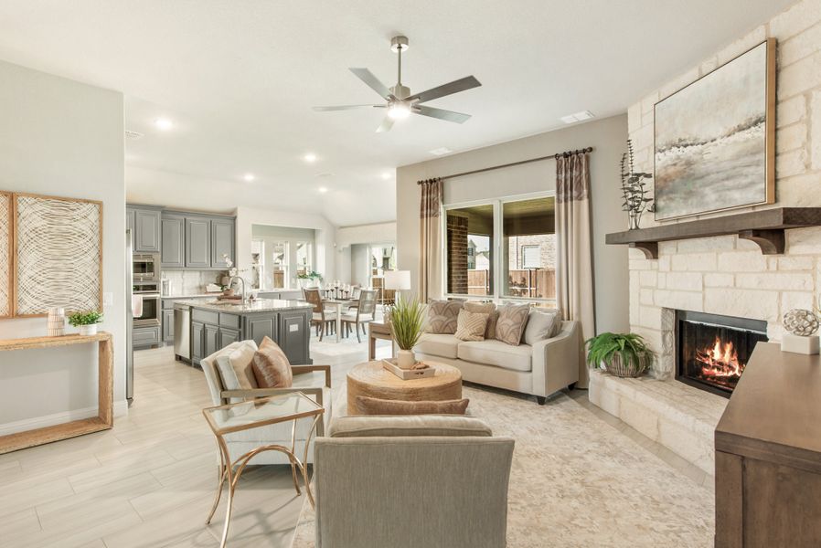Open-concept living room with stone fireplace and ceiling fan, open to kitchen with gray cabinets and island