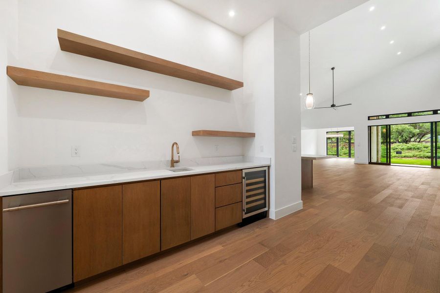 Built-in wet bar featuring wood cabinetry, white countertop, integrated sink with bronze-finish faucet, and beverage cooler