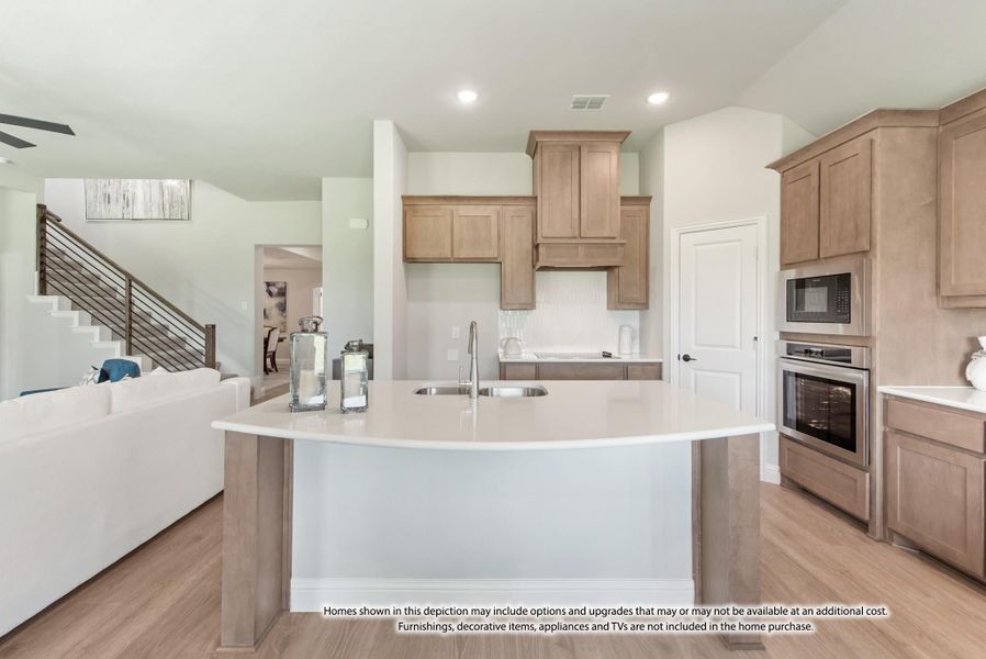 Open kitchen with large curved island, tan wood cabinets, stainless appliances, and light wood floors Open kitchen with large curved island, tan wood cabinets, stainless appliances, and light wood floors