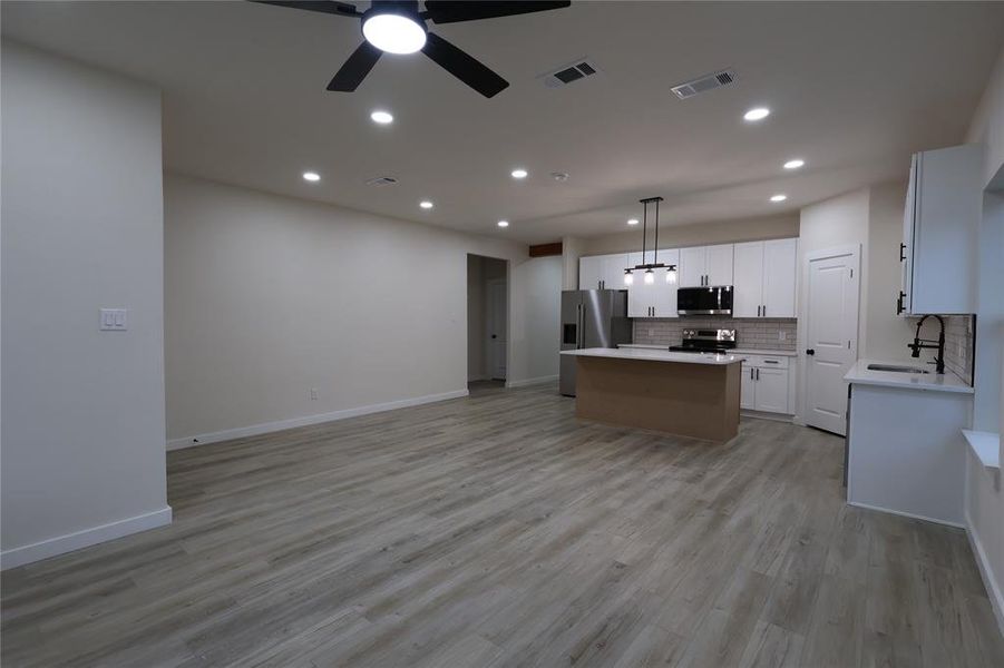 Open floor plan, hanging light fixtures, white cabinets, a center island, and backsplash