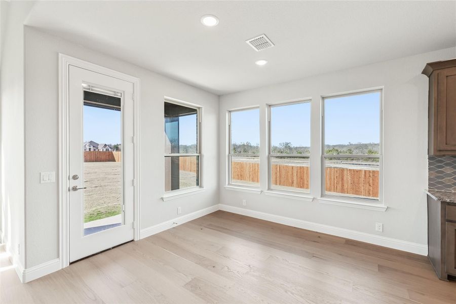 Bright dining nook with light wood floors, back door, and three windows overlooking fenced backyard Bright dining nook with light wood floors, back door, and three windows overlooking fenced backyard