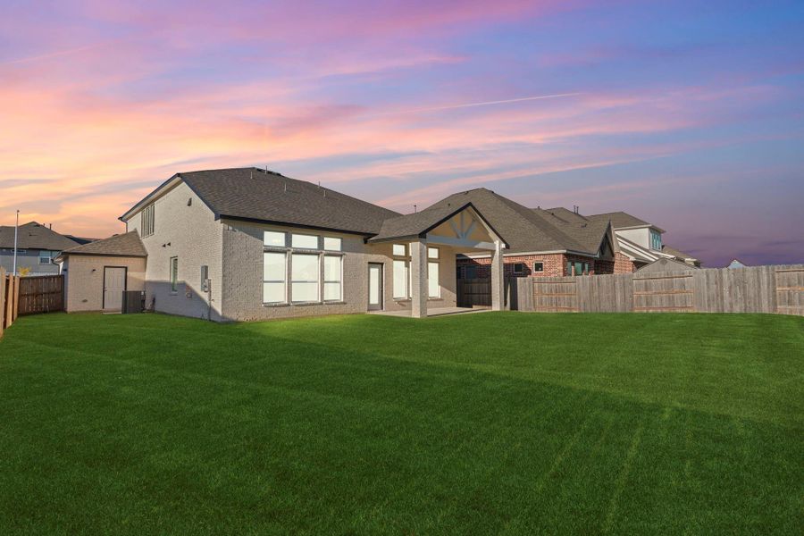 Another twilight view captures the rear of the home and its large backyard under a serene sunset sky. The all-brick exterior and covered patio create a peaceful setting for outdoor relaxation or entertaining into the evening.