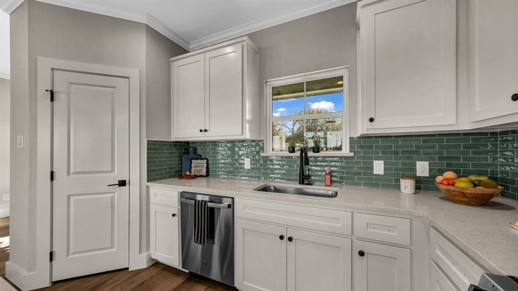 Kitchen with white cabinets, light stone countertops, stainless steel dishwasher, crown molding, and dark wood-type flooring