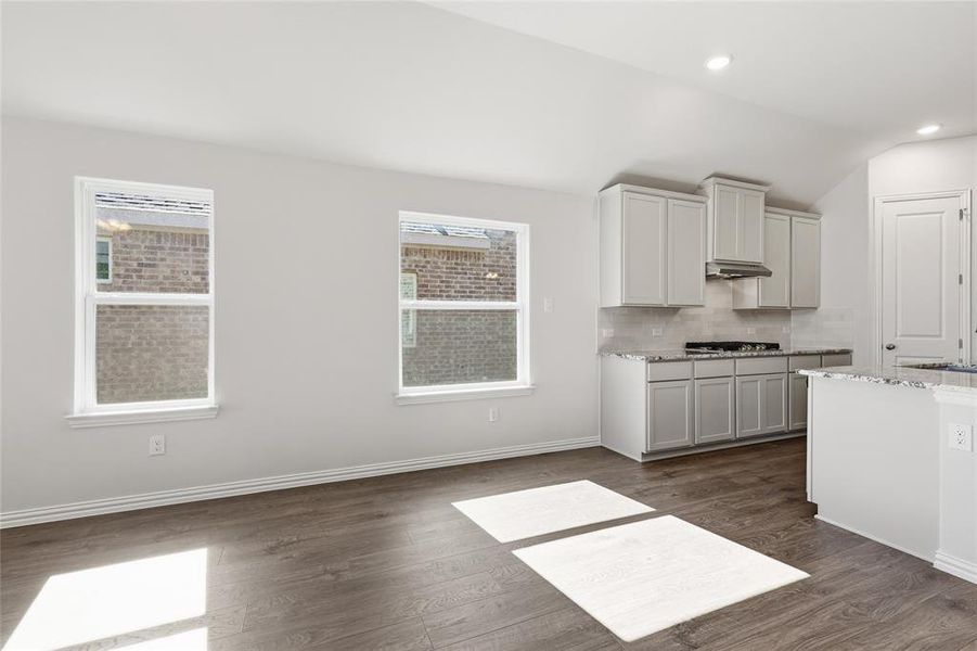 Kitchen featuring backsplash, dark wood-type flooring, light stone counters, vaulted ceiling, and recessed lighting Kitchen featuring backsplash, dark wood-type flooring, light stone counters, vaulted ceiling, and recessed lighting