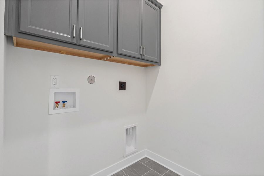 Gray upper cabinetry with chrome hardware, white walls, gray tile flooring, and white trim