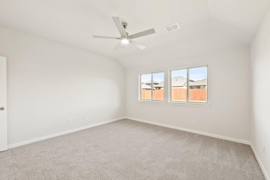 Empty bedroom with vaulted ceiling, ceiling fan, carpet flooring, and two windows with neighborhood view Empty bedroom with vaulted ceiling, ceiling fan, carpet flooring, and two windows with neighborhood view