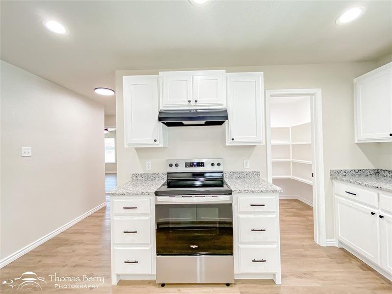 Kitchen featuring stainless steel range with electric stovetop, white cabinets, recessed lighting, light wood-style floors, and light stone counters Kitchen featuring stainless steel range with electric stovetop, white cabinets, recessed lighting, light wood-style floors, and light stone counters